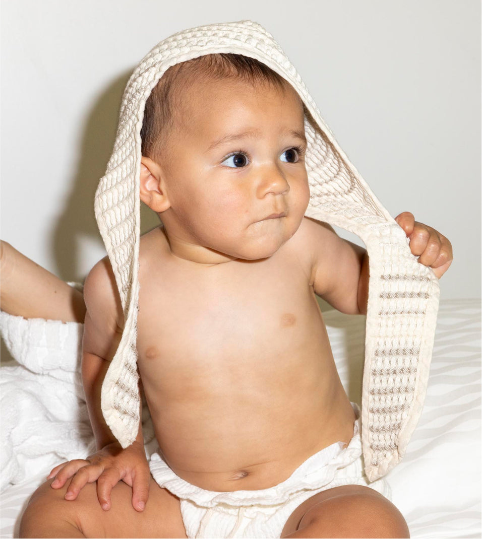 A lifestyle image of the sand baby bath bonnet modeled on baby to display form and structure