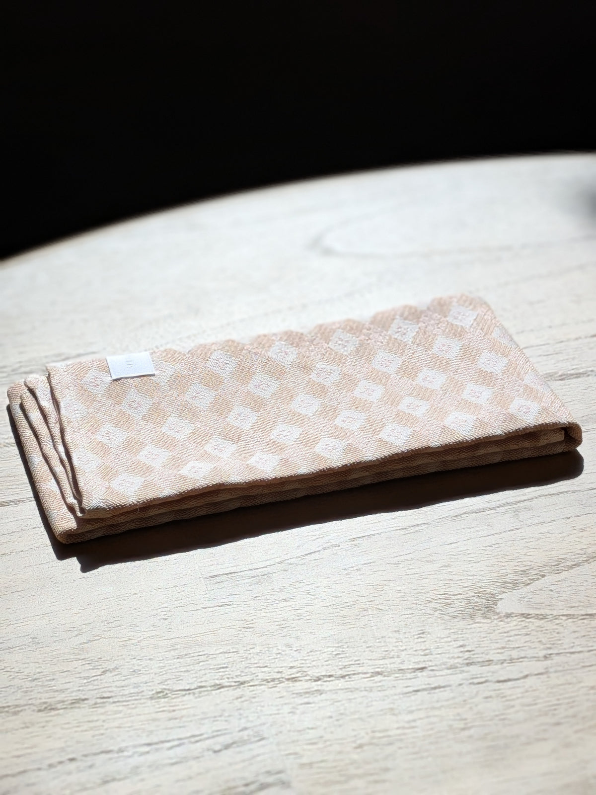 Folded Sesame diamond jacquard kitchen towel in warm sunlight on a pale oak table