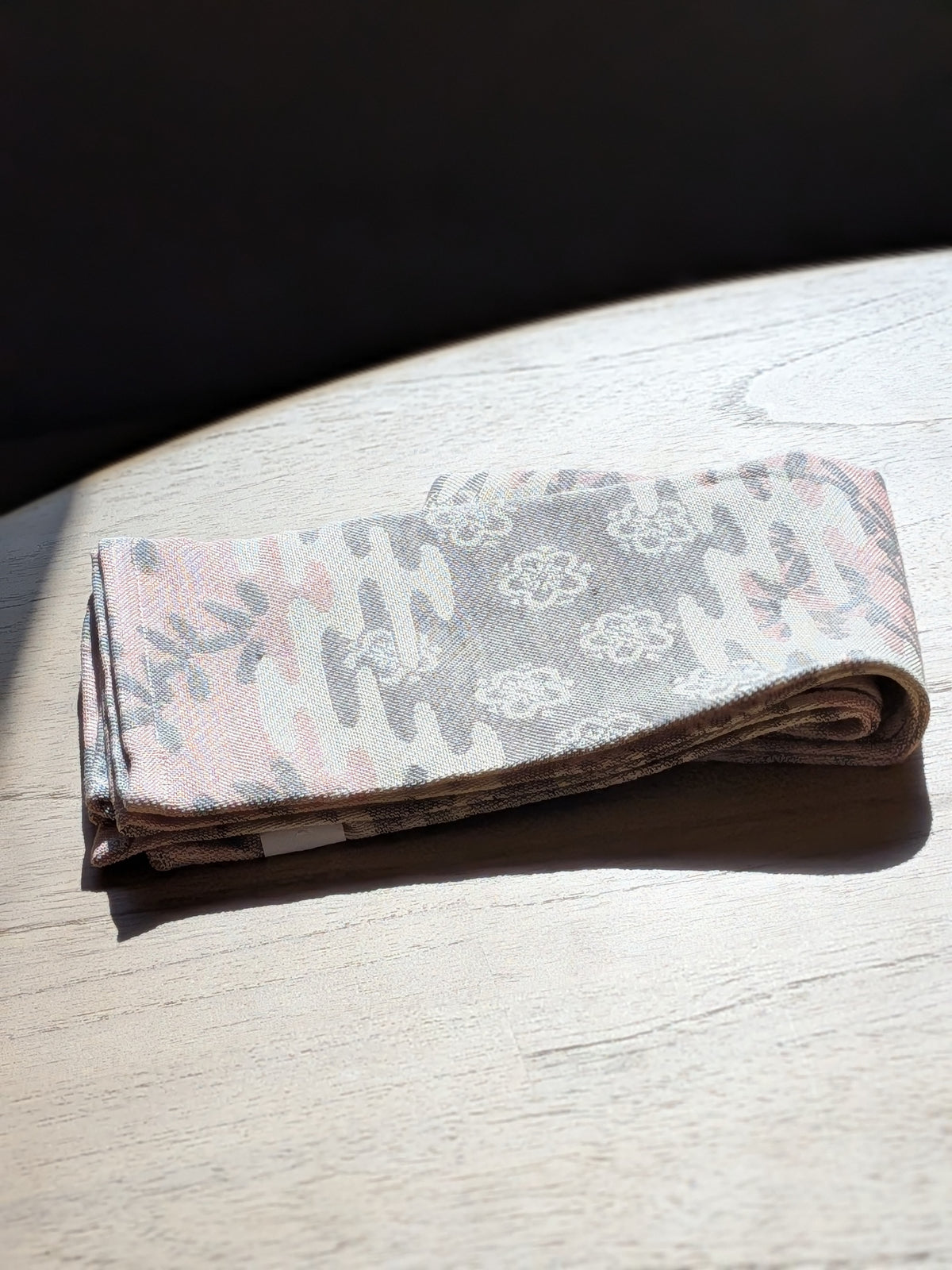 Folded Sesame/Plum plum blossom jacquard kitchen towel in pink and grey on a pale oak table